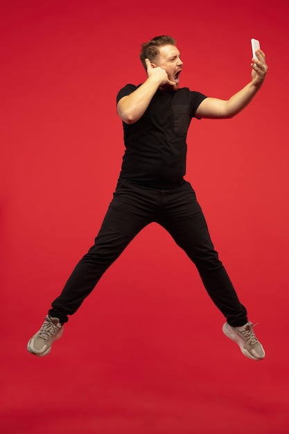 Full length portrait of young high jumping man isolated on red  wall. Male caucasian model. Copyspace. Human emotions, facial expression, sport concept.