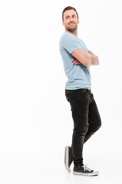 Full-length portrait of young man in casual posing with broad smile and arms folded, looking backward