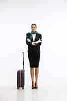 Free photo full-length portrait of young woman, stewardess with suitcase posing isolated over white backround