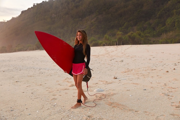 Free photo full length shot of beautiful girl surfer dressed in boardshorts and black waterproof top