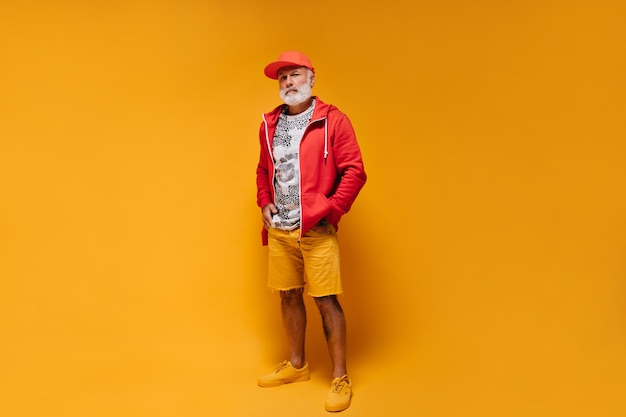 Free Photo full length shot of man in orange shorts and red jacket stylish guy with beard in stylish hoodie white leopard print tshirt and cap posing