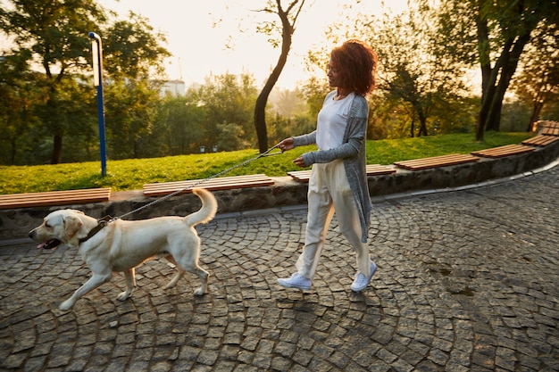 Free Photo full-length shot of pretty healthy young lady walking in the morning in park with dog