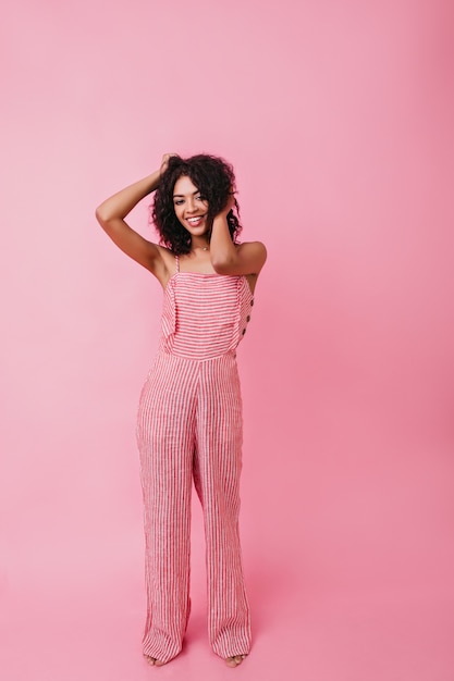 Free photo full-length shot of smiling african young woman. model straightens her curly hair .