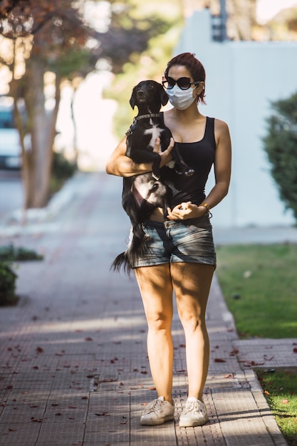 Full-length shot of a woman in a mask holding a cute puppy