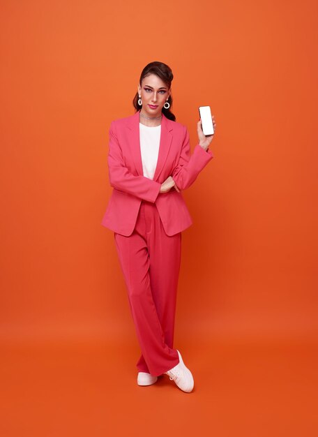 Full length smart business woman showing mobile phone blank screen isolated on orange background