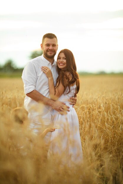 Full length stock photo of a romantic couple in white clothes hugging in the wheat field at sunset.