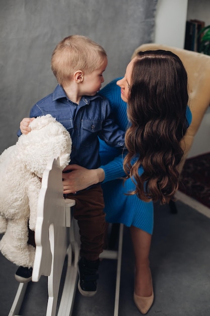 Free Photo full length studio portrait of gorgeous elegant brunette mom in denim dress with lovely laughing son on her hands they smiling at camera