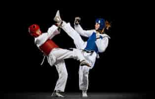 Free photo full-length studio shot of two women, taekwondo athletes training isolated over black background