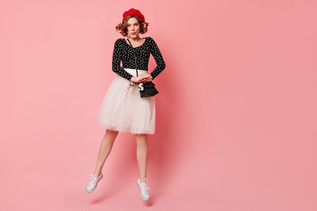 Full length view of joyful french girl in red beret. Stylish young woman in lush white skirt looking at camera.