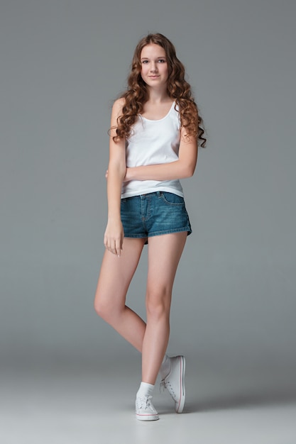 Full length of young slim female girl in denim shorts on gray wall