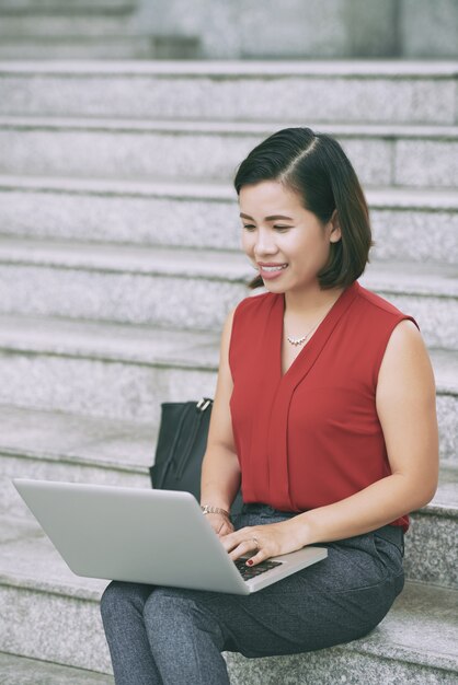 Full shot of attractive woman using laptop seated on stairs outdoors