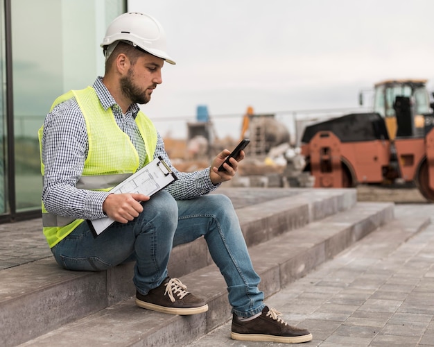 Full shot builder man sitting on stairs