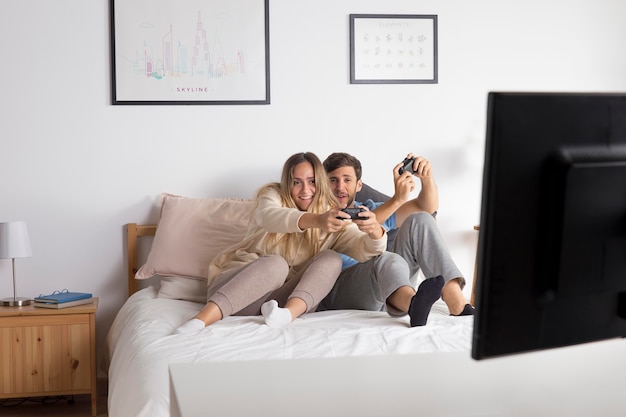 Full shot couple playing videogame in bed