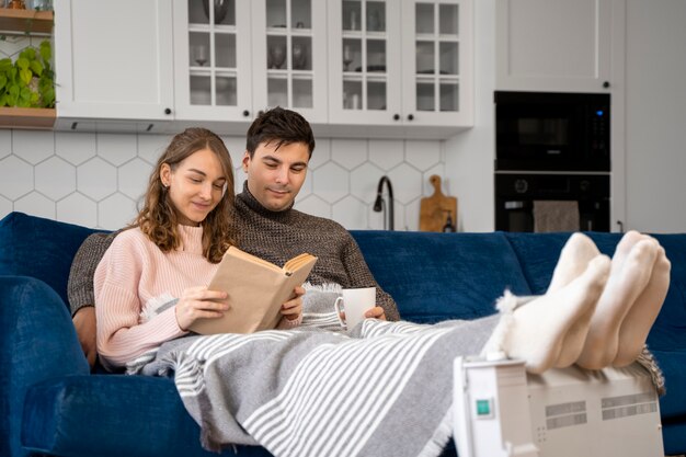 Full shot couple reading near heater