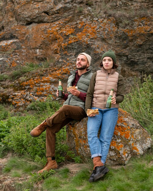 Full shot couple sitting on rock and having a drink