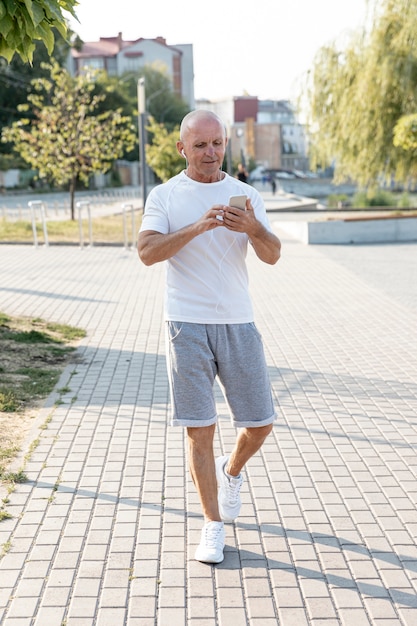 Free photo full shot elder man walking looking at his phone