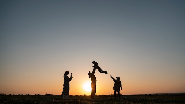 Free photo full shot family silhouette having fun at sunset