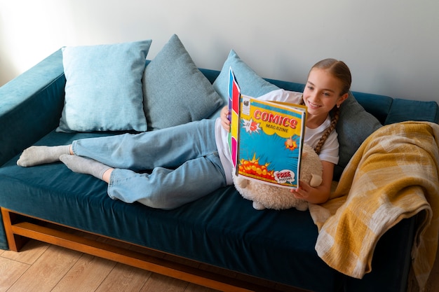 Free Photo full shot girl reading comics indoors