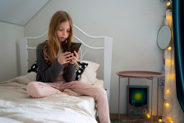 Full shot girl with smartphone in bedroom