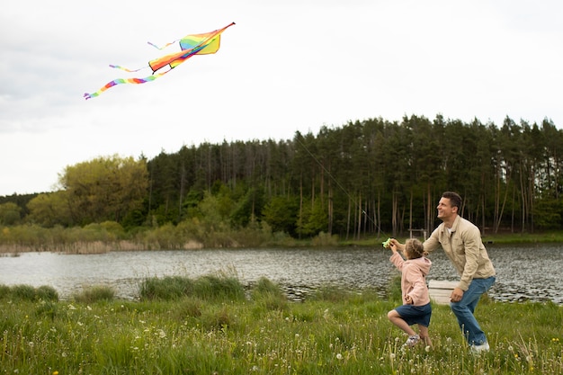 Free photo full shot happy family flying kite in nature