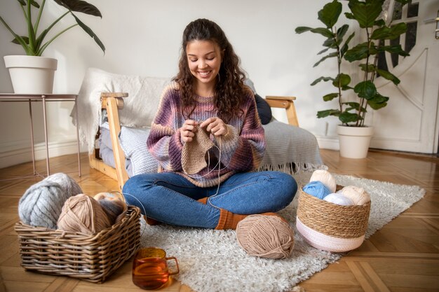 Full shot happy woman knitting at home