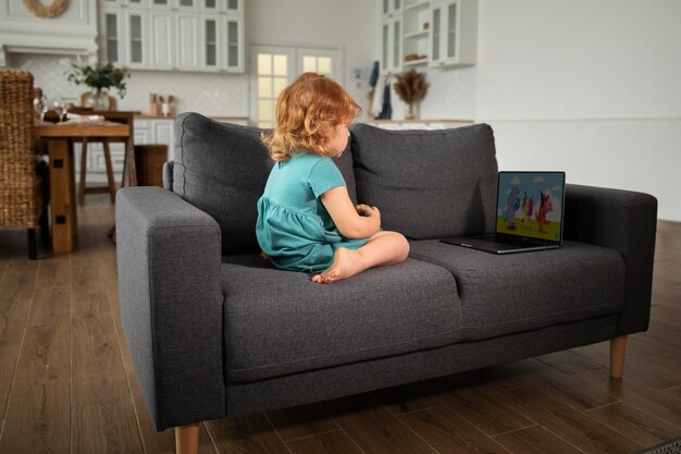 Full shot kid sitting on couch with laptop