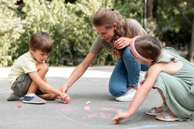 Full shot kids and teacher drawing on ground