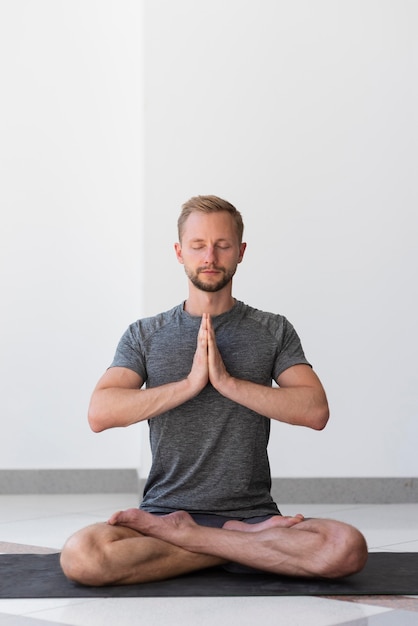 Free photo full shot man doing sukhasana pose inside on mat