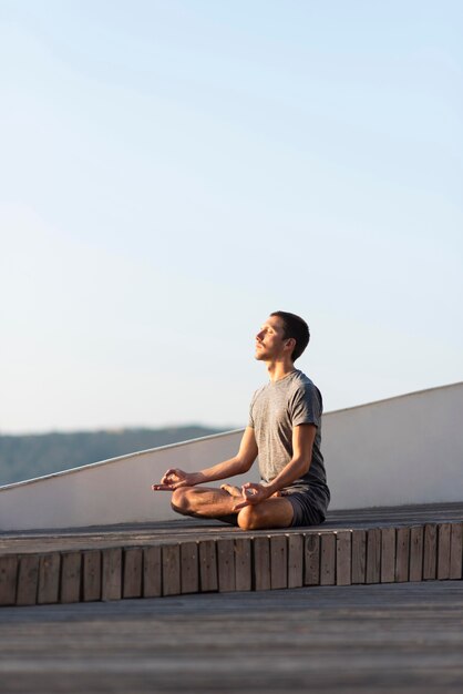 Full shot man doing sukhasana pose outdoor