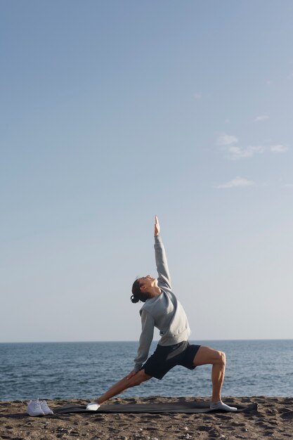 Full shot man doing yoga on beach