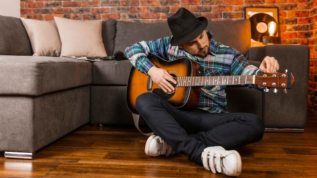 Full shot man on floor playing the guitar