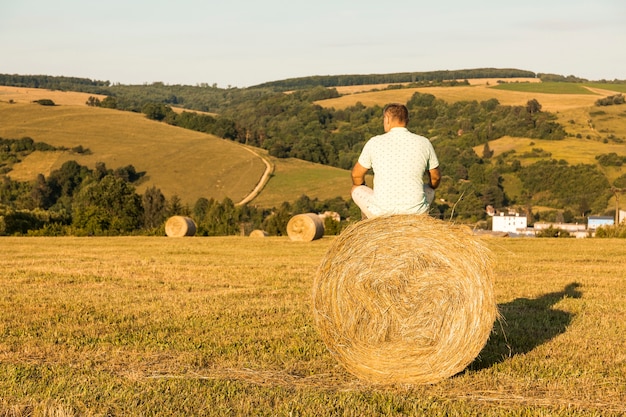 Free photo full shot man sitting on roll of hays