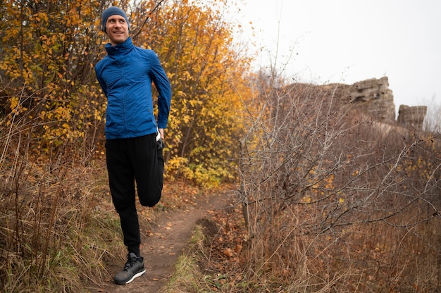 Free photo full shot man stretchig his legs in forest