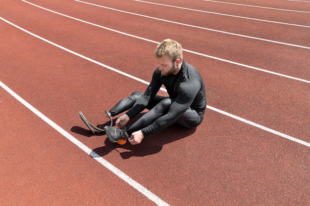 Full shot man tying shoelaces on running track