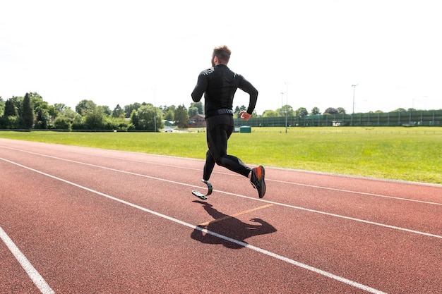 Full shot man with prosthesis running on running track