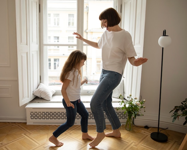 Full shot mother and girl dancing indoors