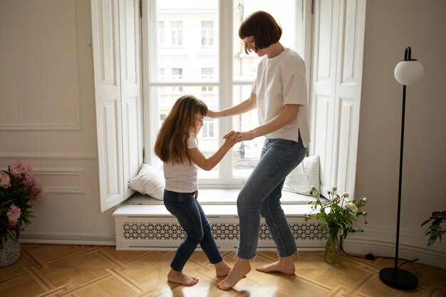 Full shot mother and girl dancing inside