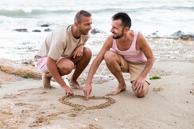 Full shot partners drawing heart on sand