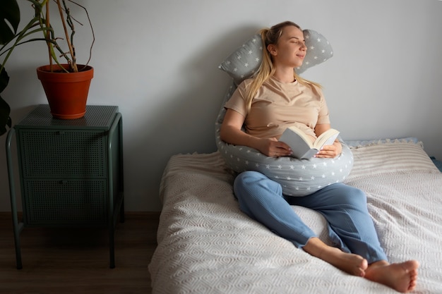 Full shot pregnant woman using nursing pillow