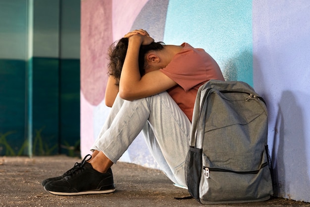 Full shot sad boy sitting on ground