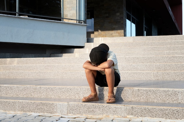 Full shot sad boy sitting on stairs