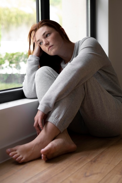 Free photo full shot sad woman near window