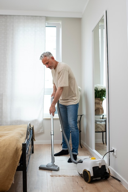 Free photo full shot senior man vacuuming the floor