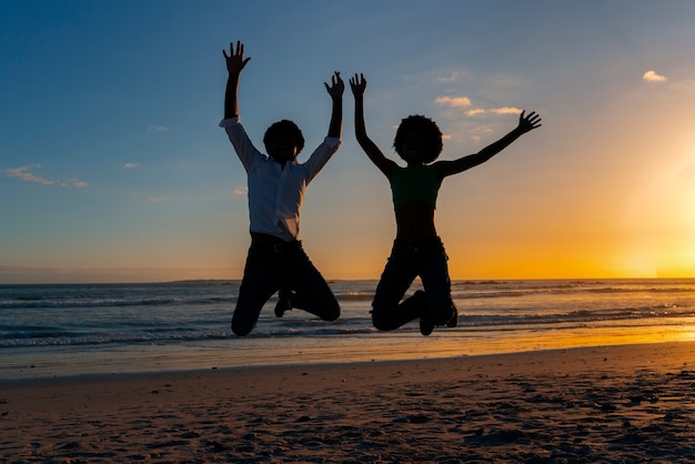 Full shot  silhouettes of people jumping at sunset