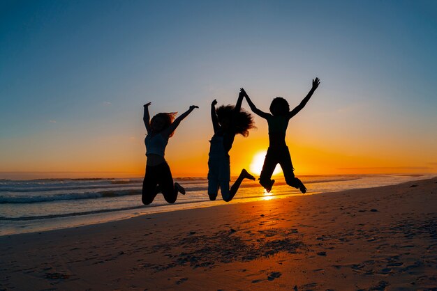 Full shot  silhouettes of people jumping at sunset