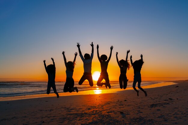 Full shot  silhouettes of people jumping at sunset