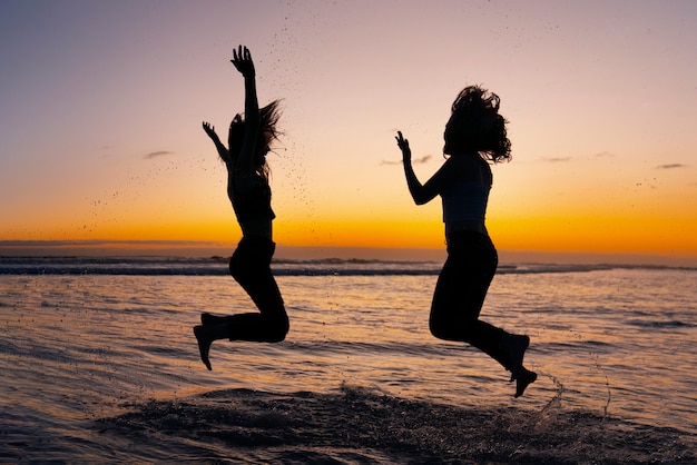 Full shot  silhouettes of people jumping at sunset