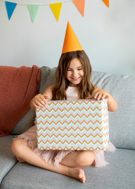 Full shot smiley girl opening present on couch