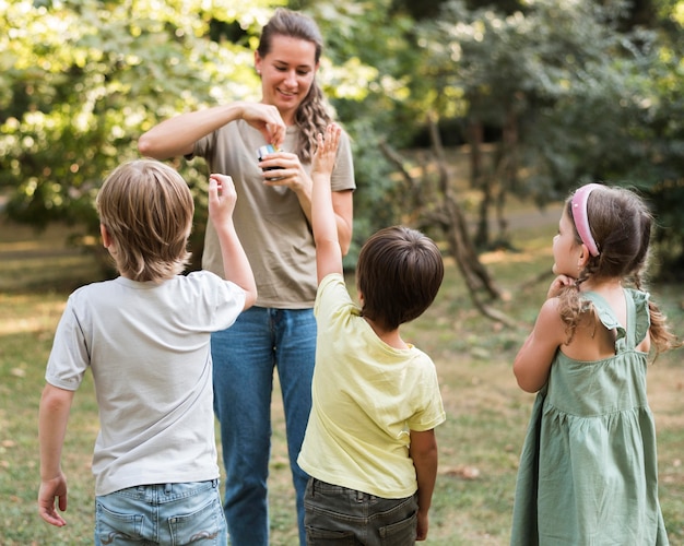 Full shot smiley teacher and kids outdoors