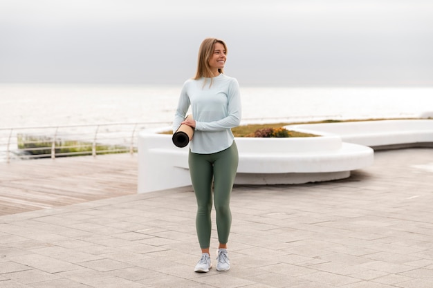 Full shot smiley woman holding yoga mat